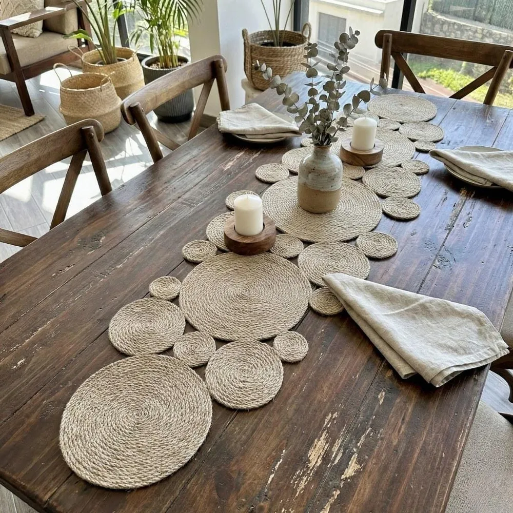 Jute table runner of coiled discs on a dark rustic dining table, with stoneware bowls, a linen napkin and eucalyptus in a vase.